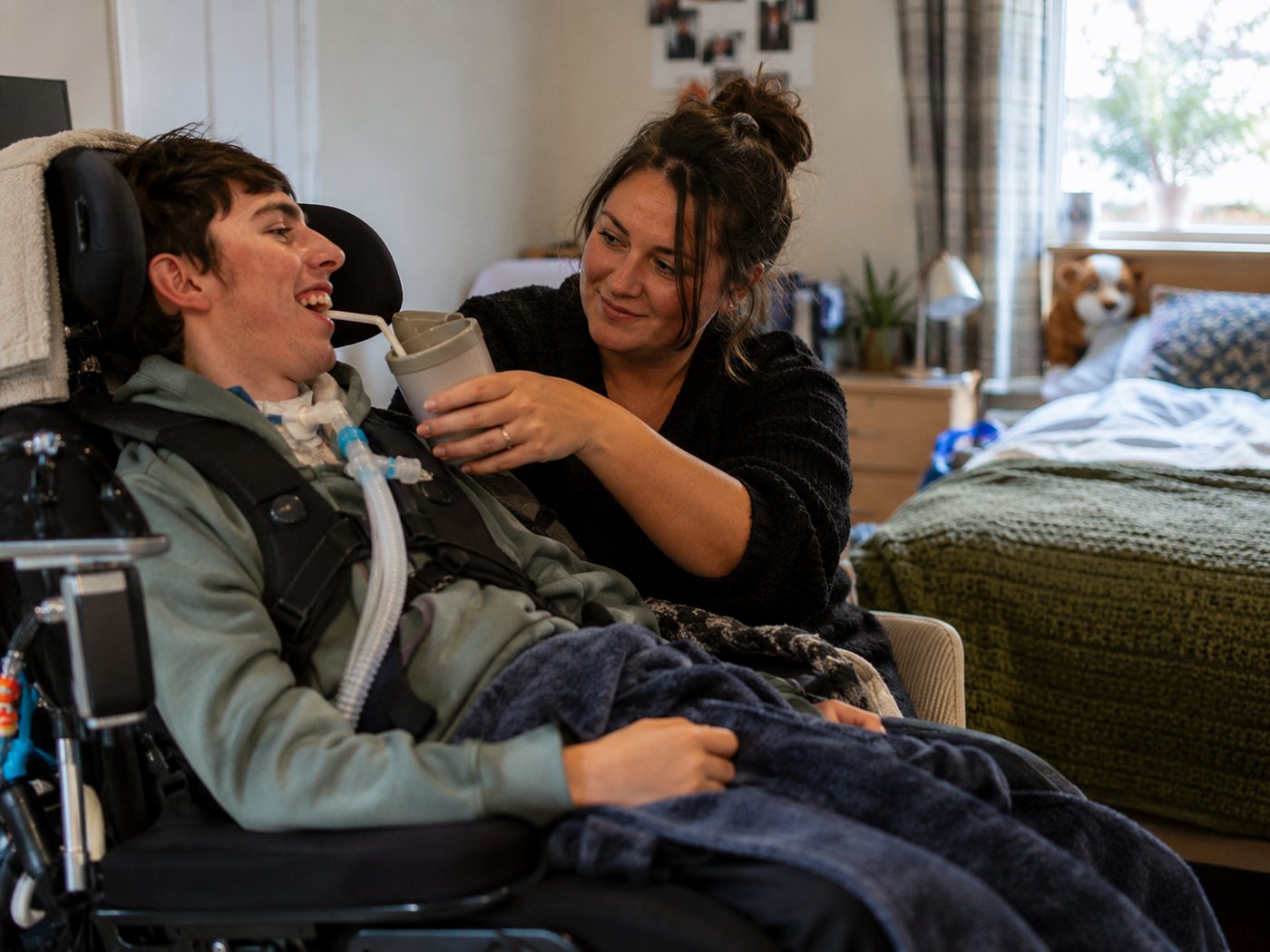 A support worker helping a young man with a tracheostomy to have a drink